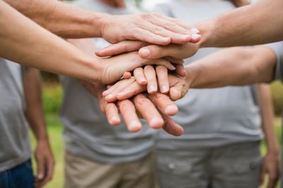 Alegre familia de voluntarios uniendo sus manos en un día soleado